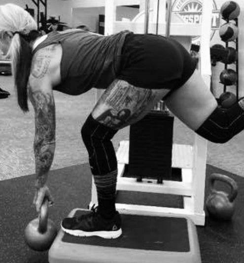 side view of woman with tattoos balancing on one leg while holding kettlebell weight